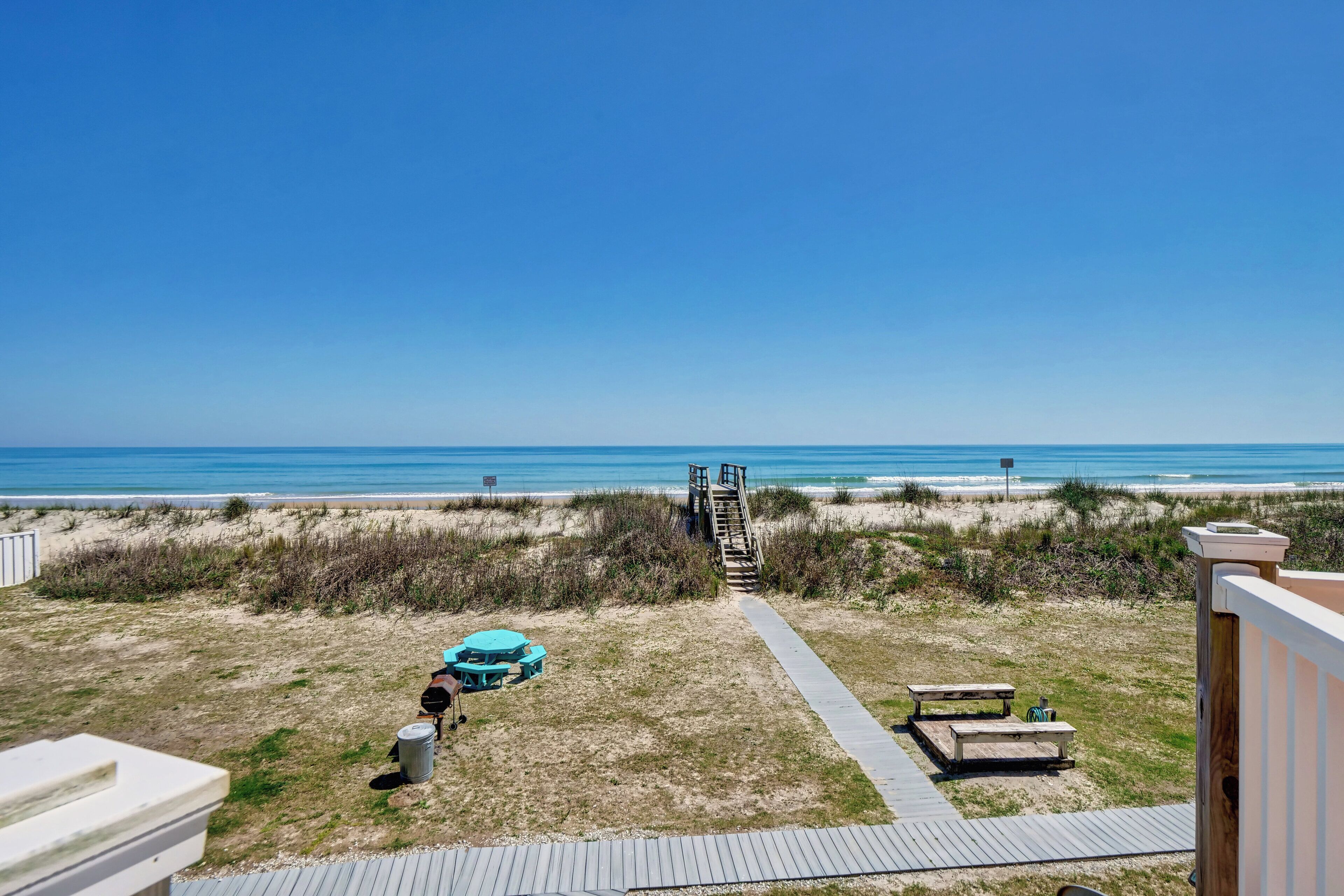 Une plage avec vue sur la mer, une terrasse en bois, des tables de pique-nique et un poste de surveillance pour les sauveteurs.