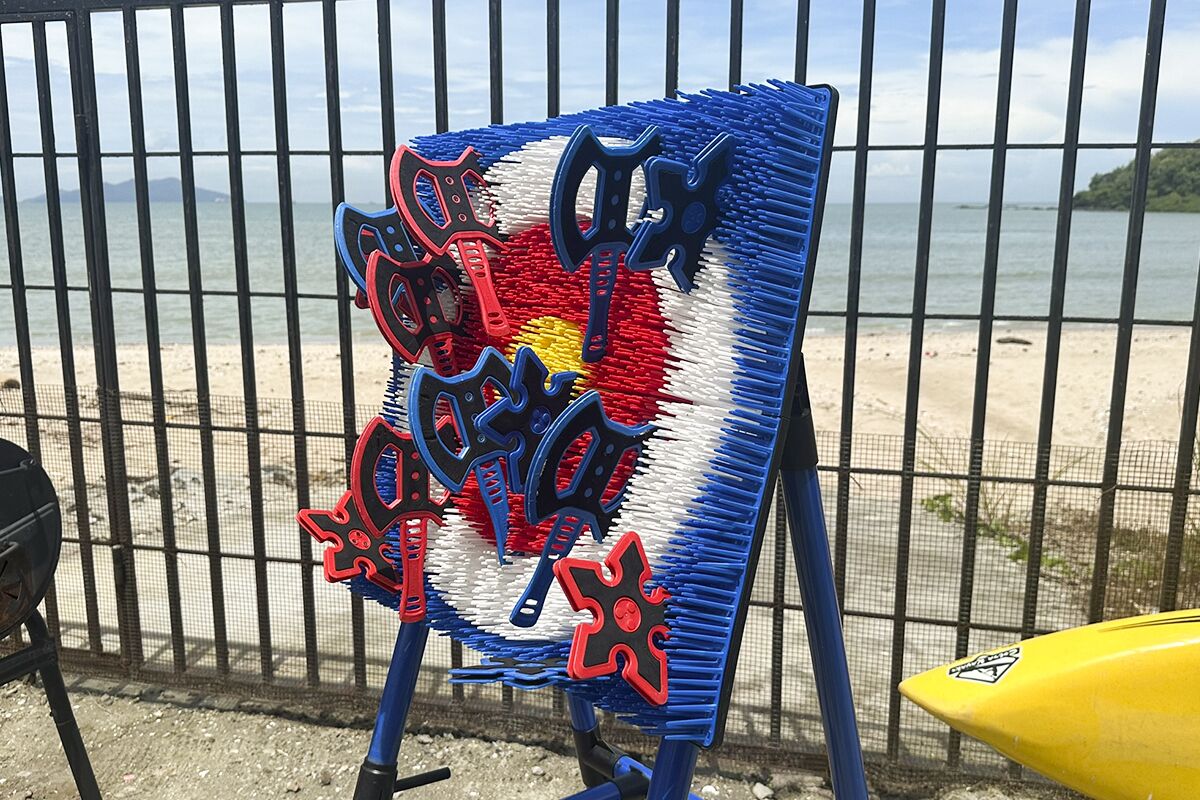 A beachside view with a fence, a yellow surfboard, and a colorful artwork on an easel.