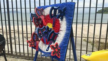 A beachside view with a fence, a yellow surfboard, and a colorful artwork on an easel.