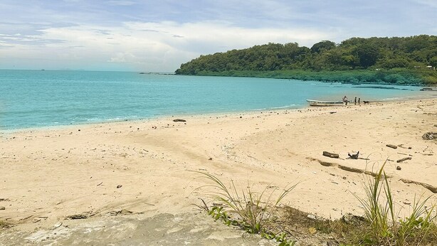 A sandy beach with clear turquoise water, a boat on the shore, and a forested hill in the background. - Excellent beach apartment with excellent amenities (Provincia de Panamá Oeste)