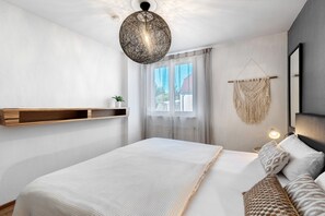 Un dormitorio moderno con una cama, mesitas de noche, decoración de macramé colgante y una ventana con cortinas.