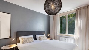 Un dormitorio con una cama grande, una lámpara de techo redonda, una ventana con cortinas y una lámpara de pared.