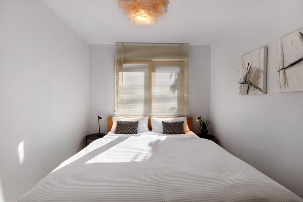 Een slaapkamer met een groot bed, twee nachtkastjes, een raam met zonwering en wanddecoratie.