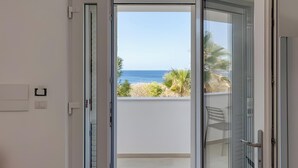 Una habitación con puerta de vidrio corrediza que da a un balcón con vista al mar y vegetación.