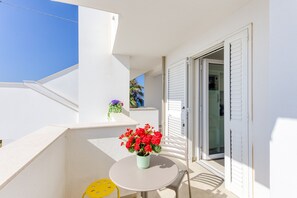 Een balkon met een witte tafel, een gele stoel en een vaas rode bloemen.