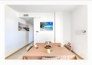 Een moderne eetkamer met een tafel gedekt voor vier personen, een schilderij met een strandthema en uitzicht op de oceaan.