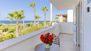 A balcony with a table, a vase of red flowers, and a view of the sea and palm trees. - Apartment 'Unit 1' with Air Conditioning (Ugento)