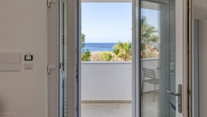 A room with a sliding glass door leading to a balcony with a view of the ocean and palm trees. - Apartment 'Unit 1' with Air Conditioning (Ugento)