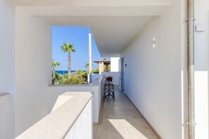 A narrow corridor with a view of the sea and palm trees, leading to a room with a window.