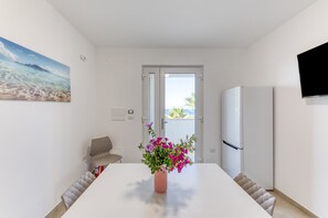 A modern kitchen with a white table, a vase of flowers, a refrigerator, and a painting on the wall.