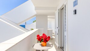 Een balkon met een tafel, een bloevas, een deur en een bord aan de muur.