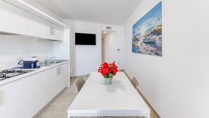 Een moderne keuken met witte kastjes, een inbouwfornuis en een eethoek met een witte tafel en stoelen.