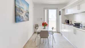 Een moderne keuken met witte kasten, een eettafel met stoelen en een schilderij aan de muur.