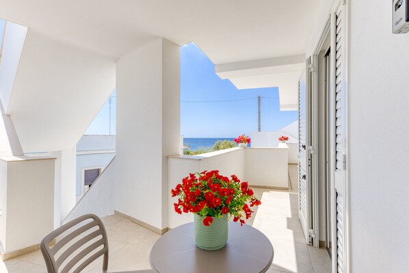 A balcony with a table, chair, and a vase of red flowers.