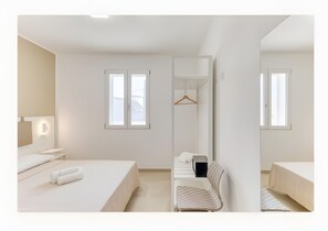 A modern hotel room with a bed, a chair, a desk, and a wardrobe.