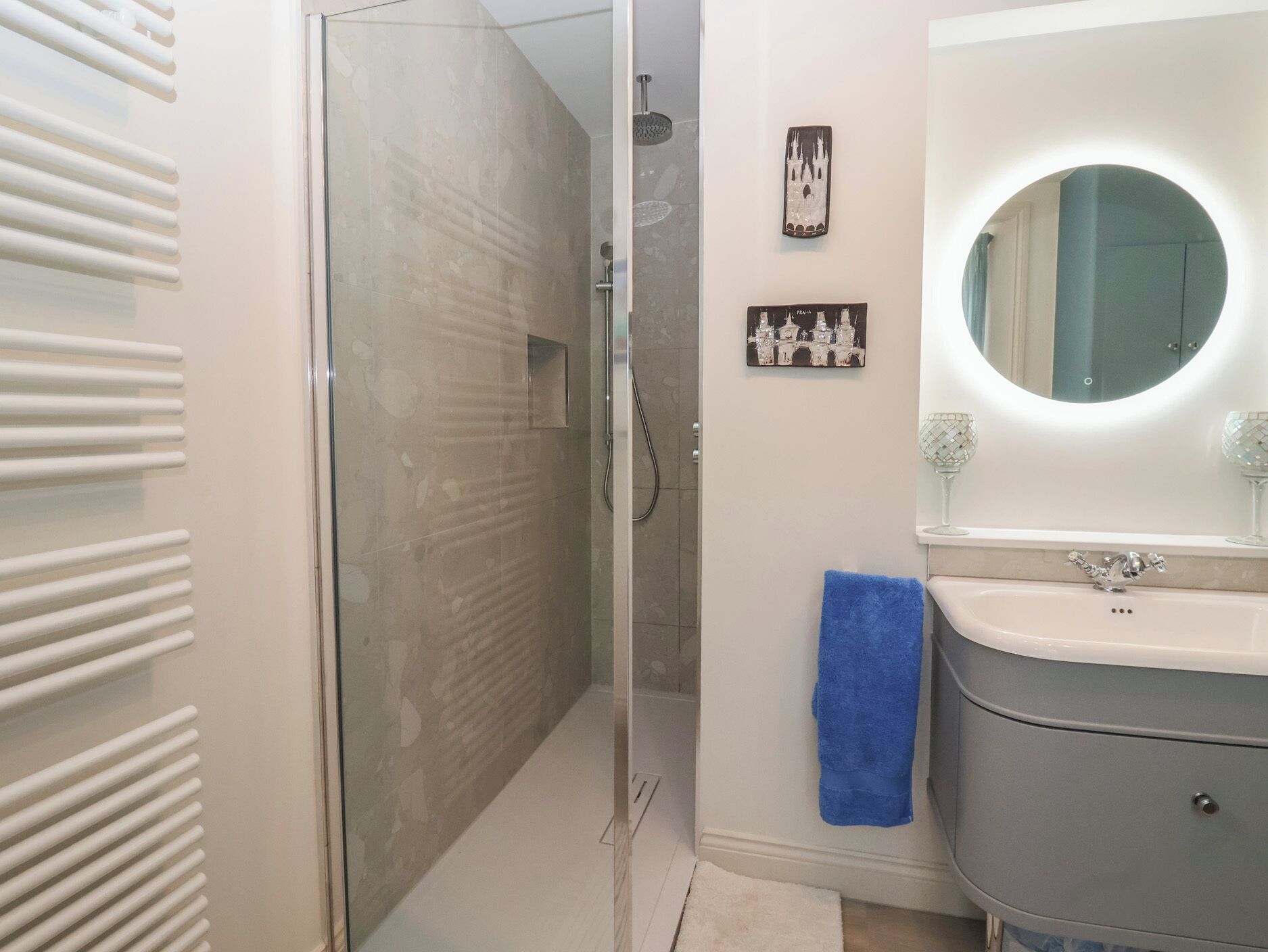 A bathroom with a glass shower enclosure, a sink with a mirror, and a blue towel hanging on the wall.