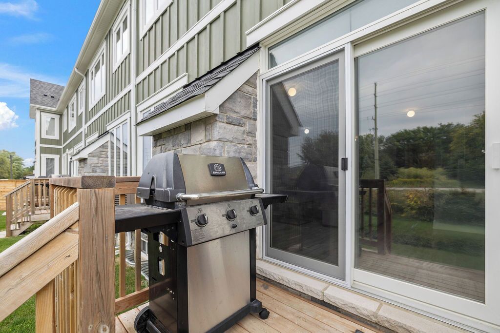A patio with a stainless steel grill, wooden deck, and a house with stone accents and large sliding glass doors.