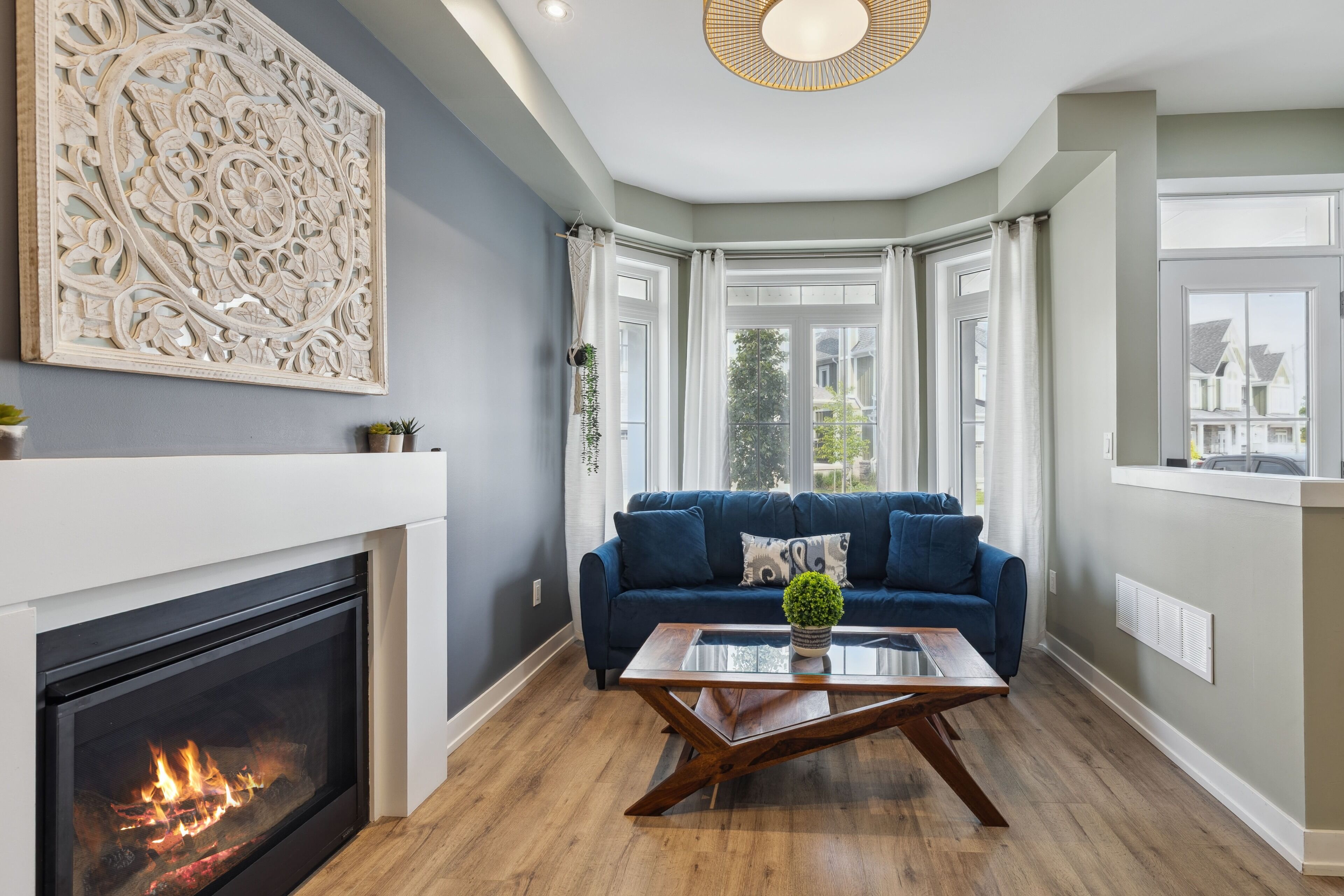 A modern living room with a fireplace, a blue sofa, and a glass coffee table.