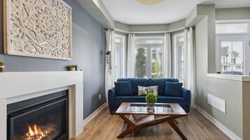 A modern living room with a fireplace, a blue sofa, and a glass coffee table.