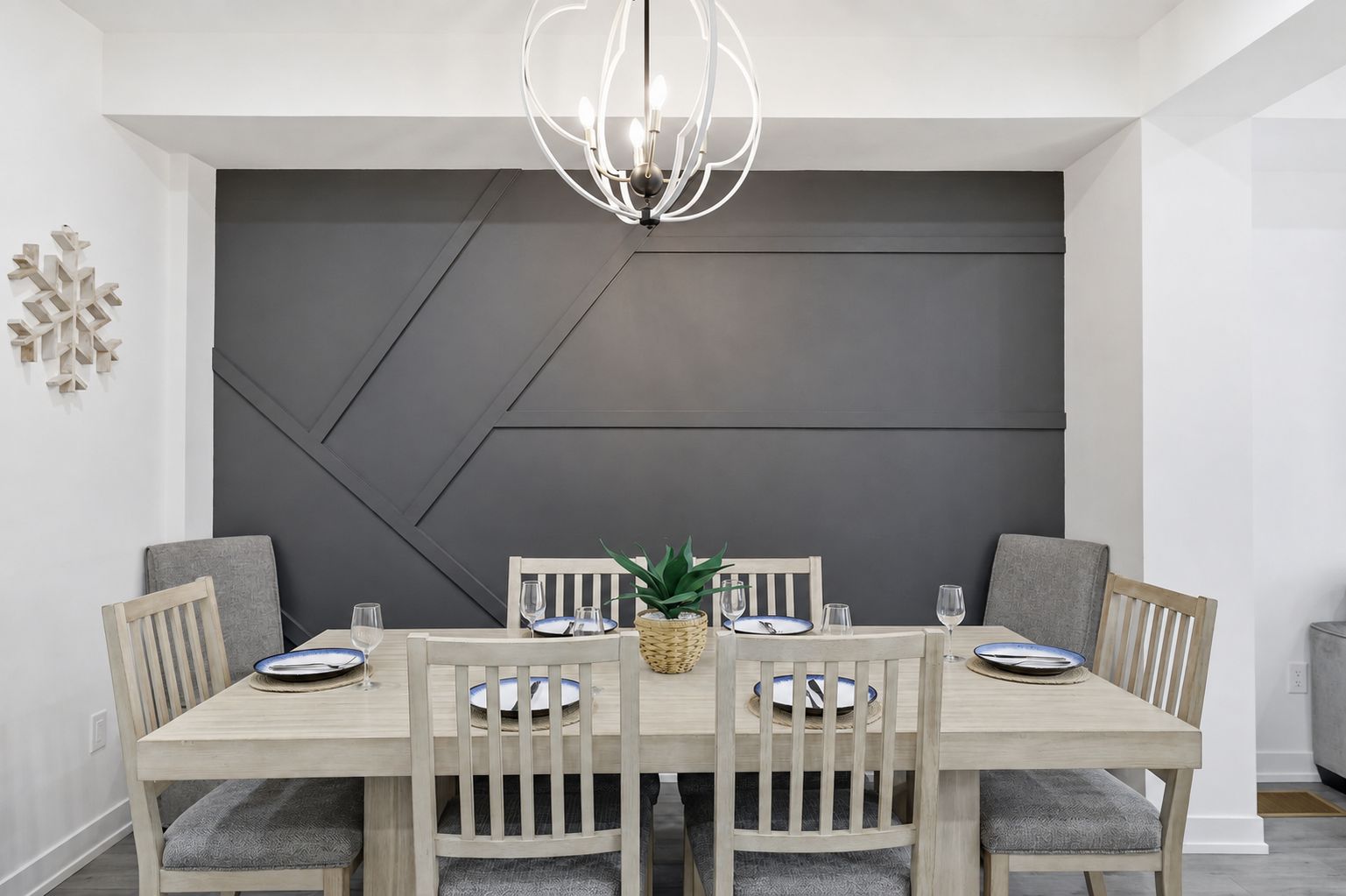 En matplats med en modern kristallkrona, en stor, mörk accentvägg och ett träbord med plats för fyra personer.