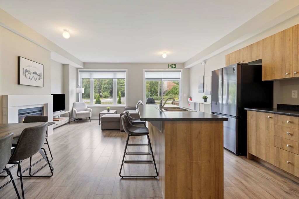 A modern kitchen with a central island, bar stools, a dining area with a TV, and a fireplace.