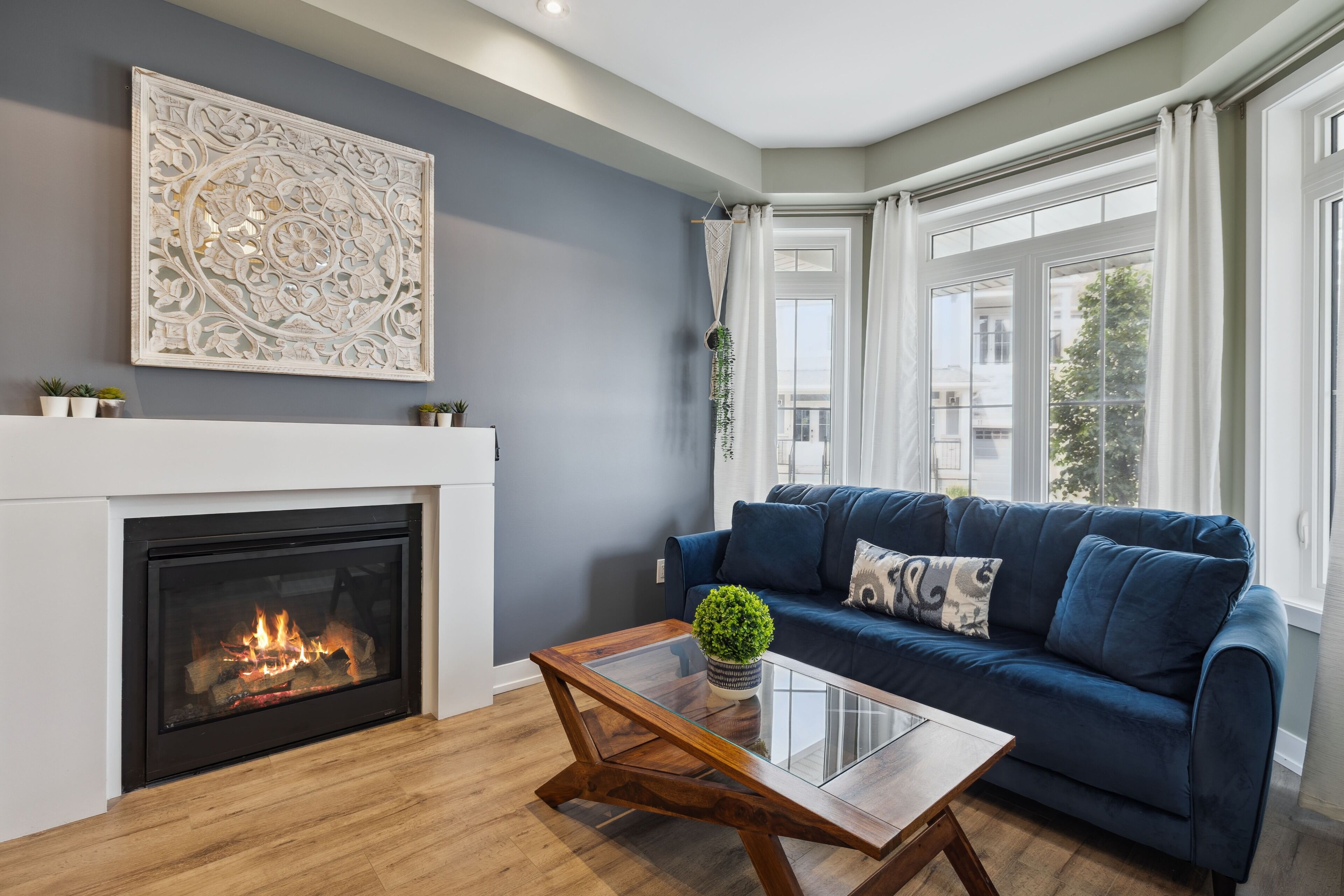 A living room with a fireplace, a blue sofa, a glass coffee table, and a decorative wall piece.