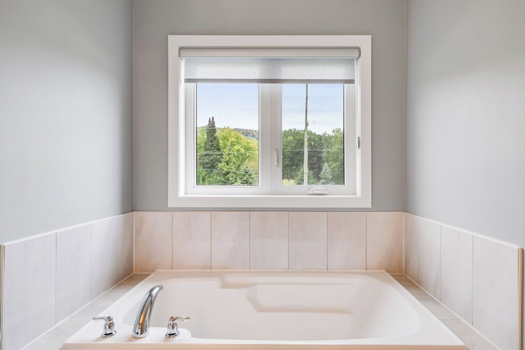 Un baño moderno con una bañera grande, una ventana con vistas a la vegetación y un suelo de baldosas de color claro.