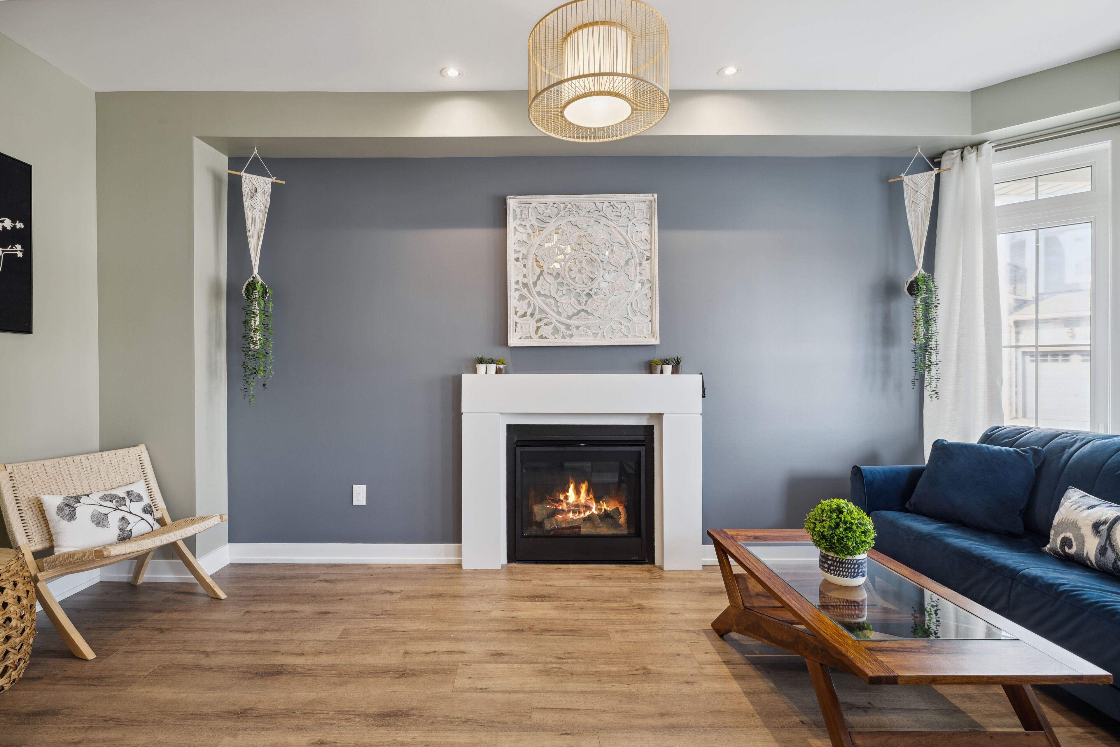 Una sala de estar con chimenea, un sofá azul, una mesa de centro de madera y una planta de macramé colgante.