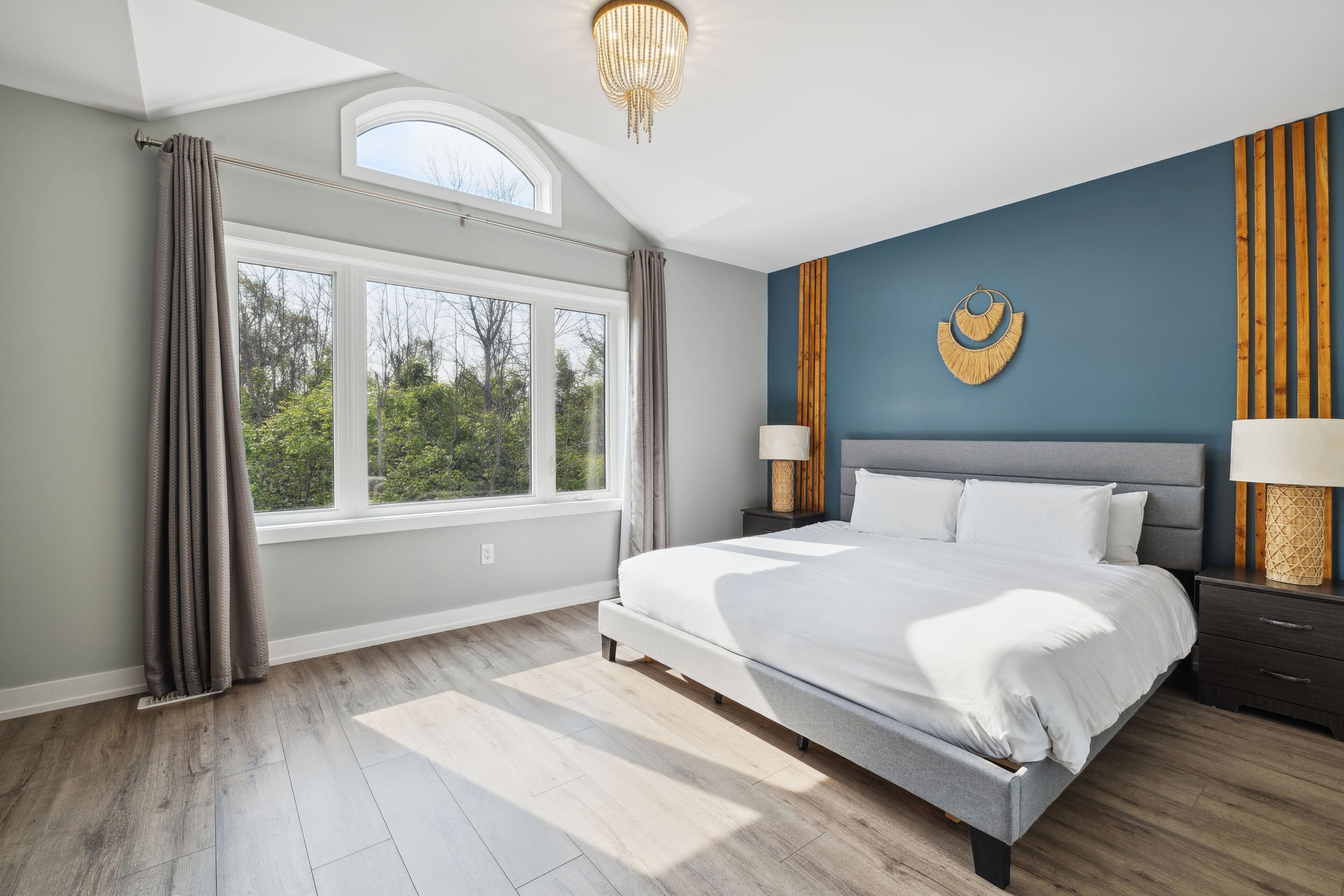 A bedroom with a large bed, a skylight, a view of trees, and a decorative wall piece.