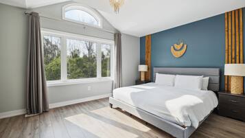 A bedroom with a large bed, a skylight, a view of trees, and a decorative wall piece.
