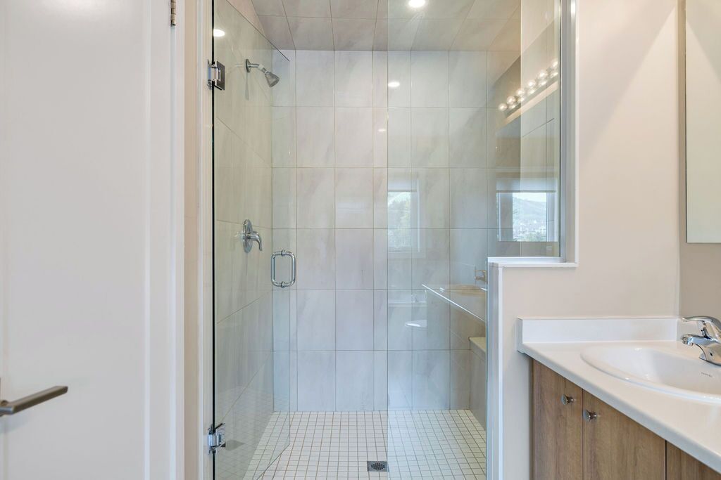 Een moderne badkamer met een douchecabine van glas, een witte wastafel en een houten opbergmeubel.