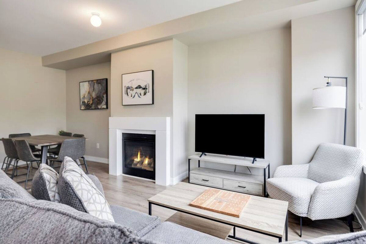 A modern living room with a fireplace, a flat-screen TV, a dining area, and a comfortable seating arrangement.