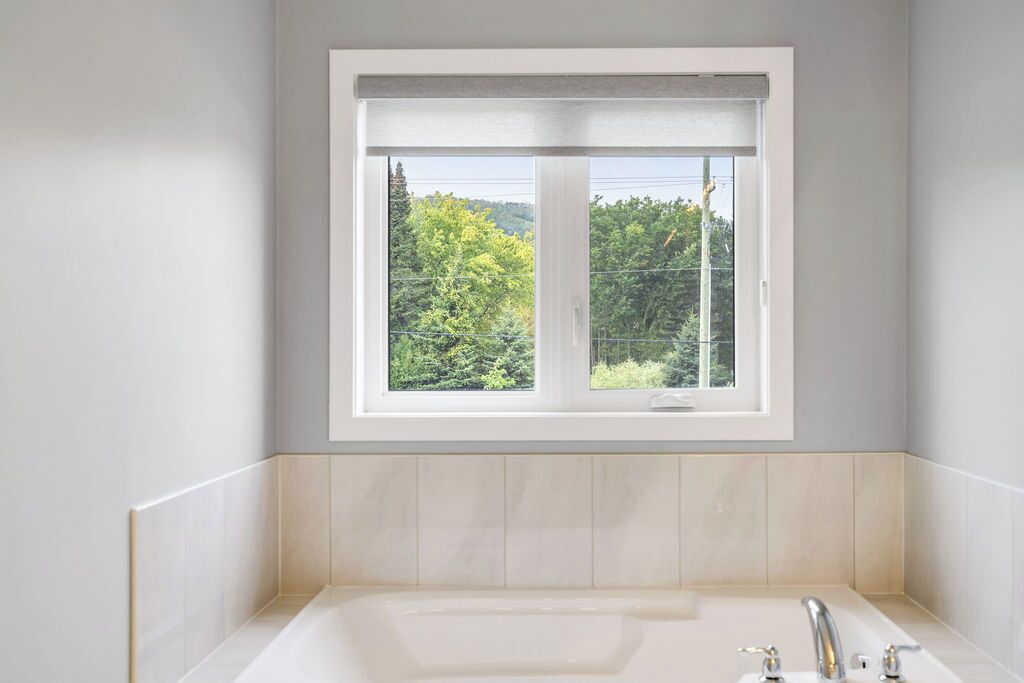 Une salle de bain dotée d’une grande fenêtre, d’une baignoire et offrant une vue sur la verdure environnante.