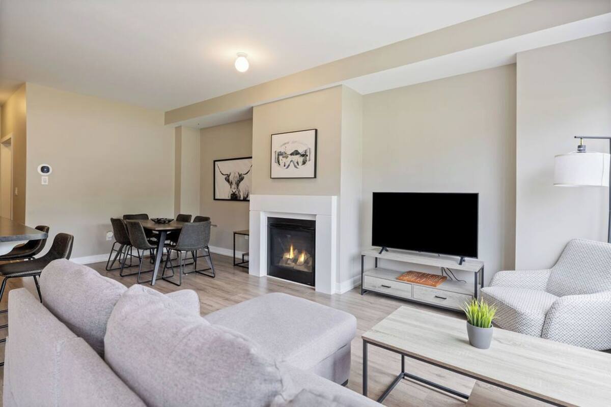 A modern living room with a fireplace, a flat-screen TV, a dining area, and a sofa.