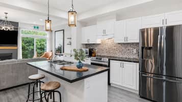 Una cocina moderna con armarios blancos, un refrigerador de acero inoxidable y una isla central con taburetes.
