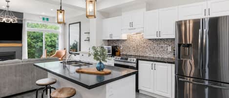 A modern kitchen with white cabinetry, a stainless steel refrigerator, and a central island with stools.