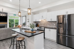 Una cocina moderna con armarios blancos, un refrigerador de acero inoxidable y una isla central con taburetes.