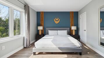 Una camera da letto con un letto grande, due comodini con lampade, un elemento decorativo appeso al muro e una finestra con tende.