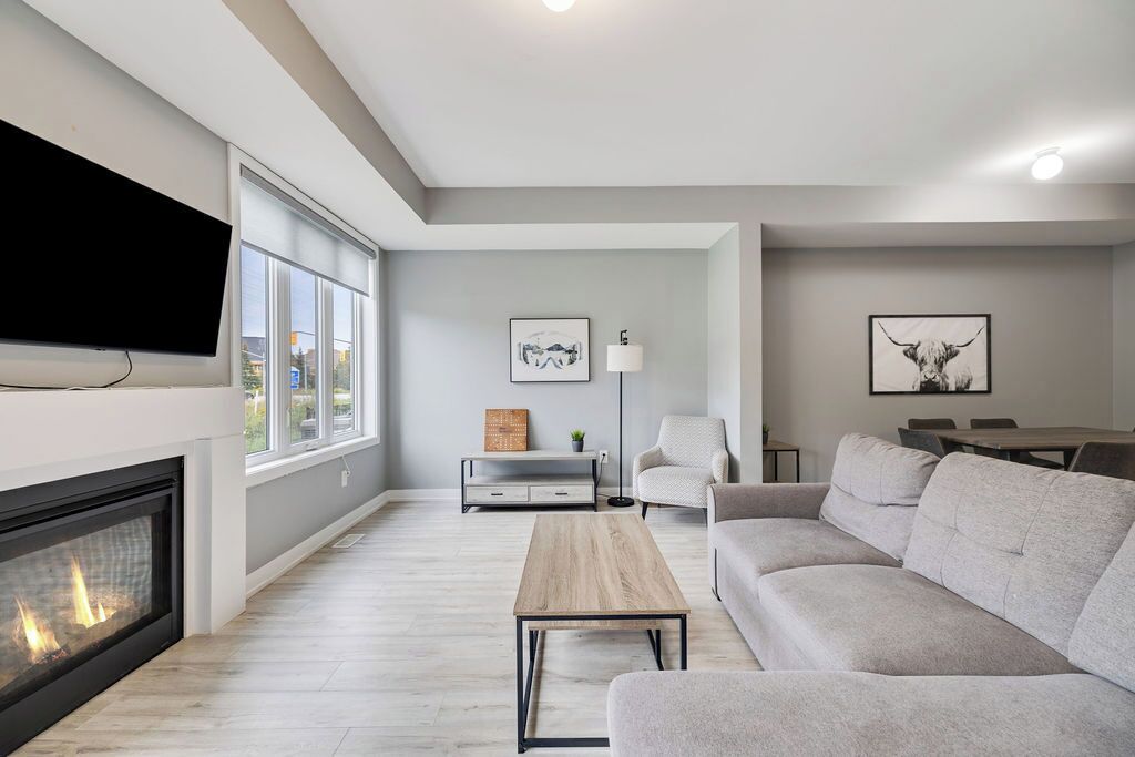 Een moderne woonkamer met een open haard, een grijze bank, een houten salontafel en kunstwerken aan de muur.