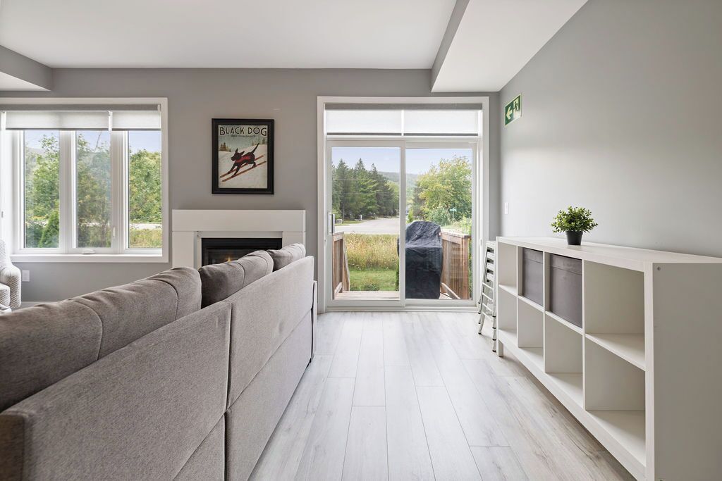 A modern living room with a grey sofa, a fireplace, and a large sliding glass door leading to a garden.