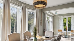 A dining area with a large table set for six, surrounded by chairs, with a view of trees through large windows. - Crosswinds Townhomes (The Blue Mountains)