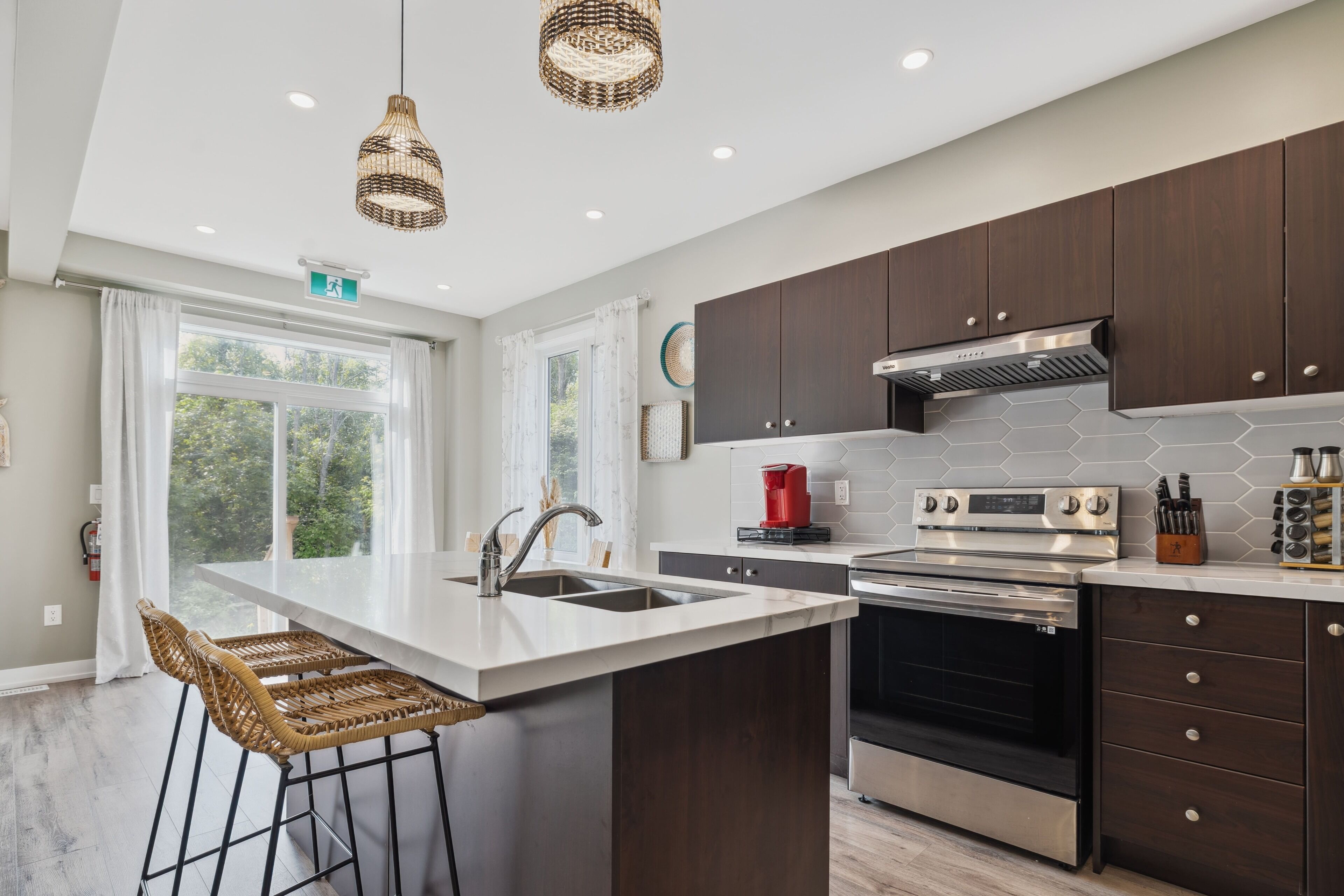 A modern kitchen with dark wooden cabinets, a large island with a sink, and stainless steel appliances.