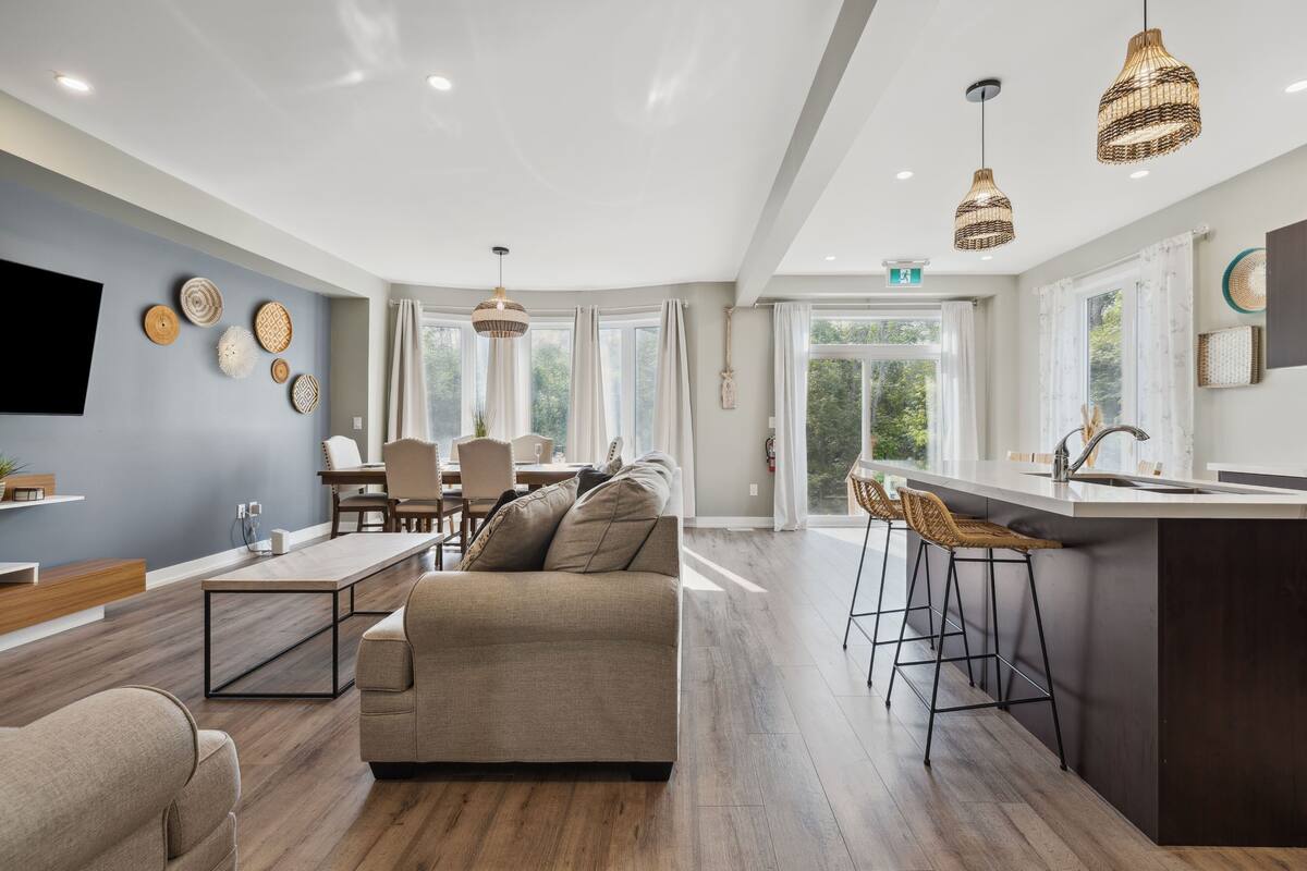 A modern kitchen with a central island, bar stools, and a dining area with a sofa and chairs.