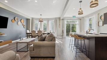A modern kitchen with a central island, bar stools, and a dining area with a sofa and chairs.