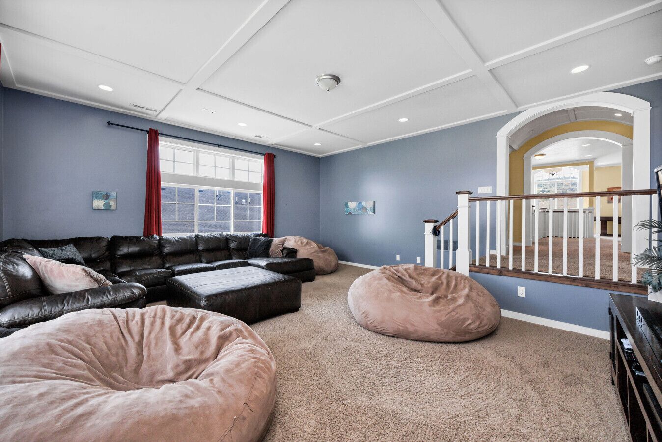 Un salon spacieux avec un canapé d’angle, un grand pouf et un escalier menant à un niveau supérieur.