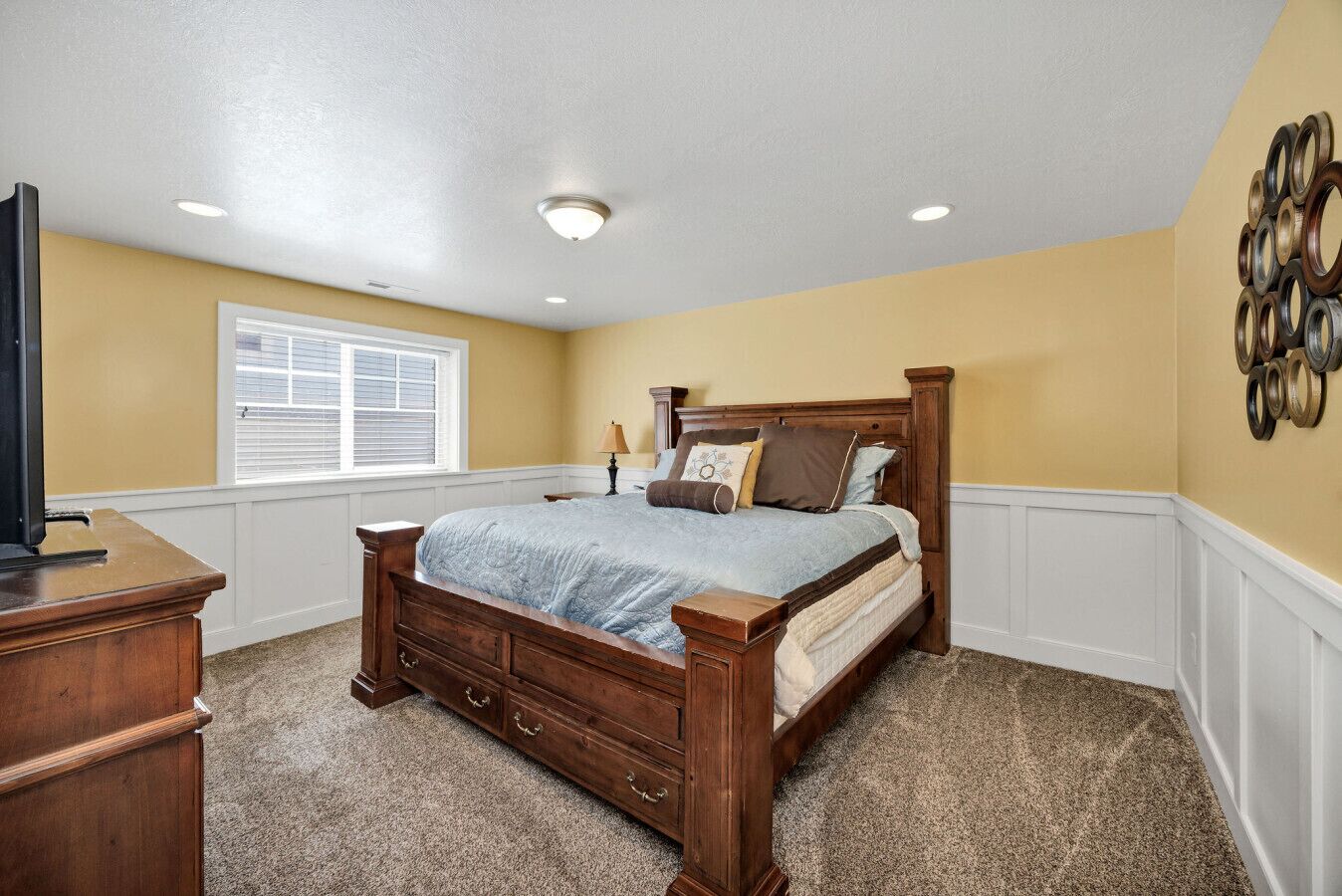 A bedroom with a wooden bed, a nightstand, a dresser, and a window with blinds.