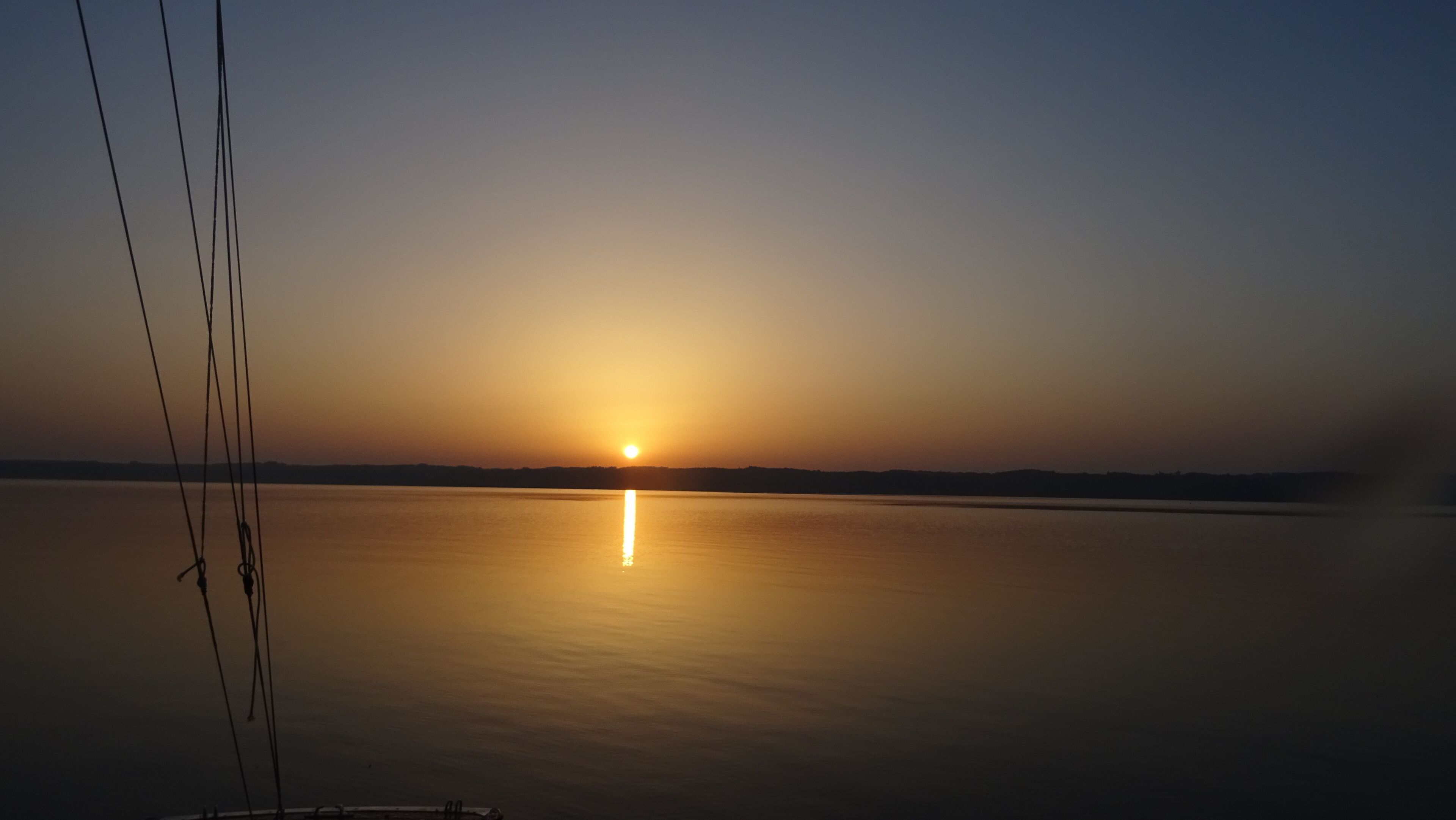 Ein Sonnenuntergang über ruhigem Wasser mit einer fernen Küstenlinie.