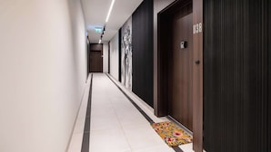Un pasillo moderno de hotel con piso de baldosas, una puerta de madera con el número 038 y un cuadro abstracto blanco y negro en la pared.