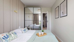 Una habitación de hotel moderna con una cama grande, una mesita de noche, una pequeña planta en maceta y una bandeja con tazas y una tetera.