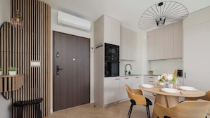 Una cocina moderna con armarios blancos, horno empotrado y comedor con una mesa y sillas de madera redondas.